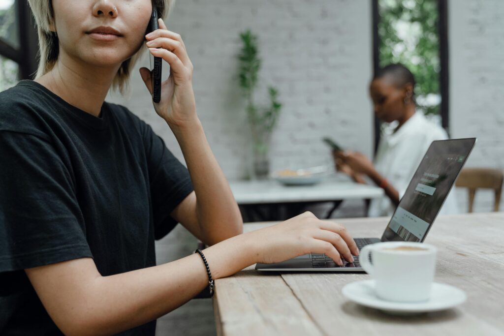 People working remotely in a modern café, using laptops and phones for business tasks.