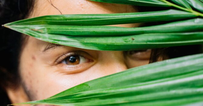 Portrait of a smiling woman partially obscured by lush green leaves.